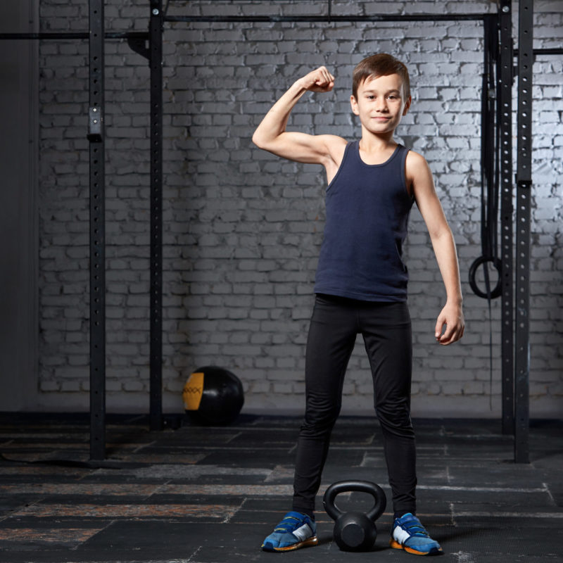 Training and sport. Kid in crossfit gym shows his muscles. Healthy lifestyle.